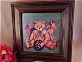 A charming picture of old fashioned toys appearing to be painted on wooden slats. This print features a teddy bear, ball, kite, and rocking horse framed under glass.