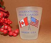 Frosted glass shot glass, jigger, with red white and blue heat bonded transfer with Canada and USA flags reading "International Peace Garden"