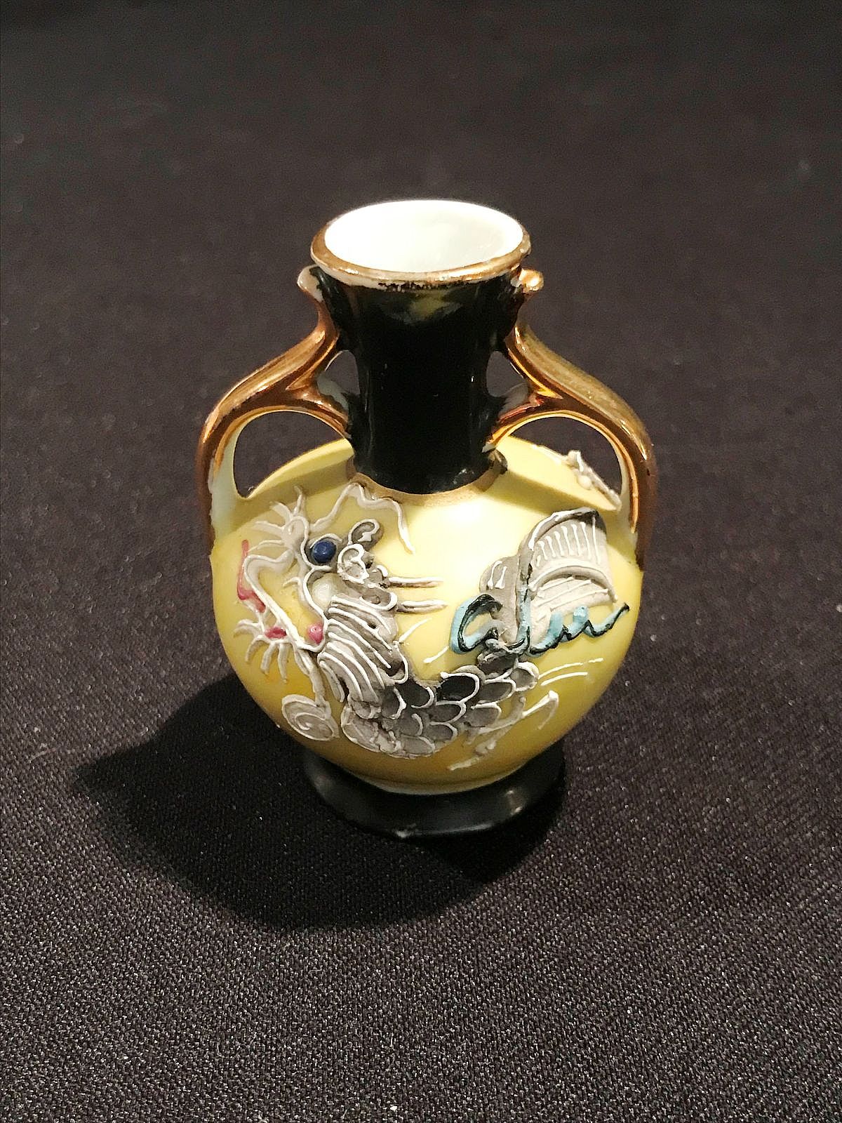 a small, vintage ceramic vase featuring raised, textured dragons and other designs