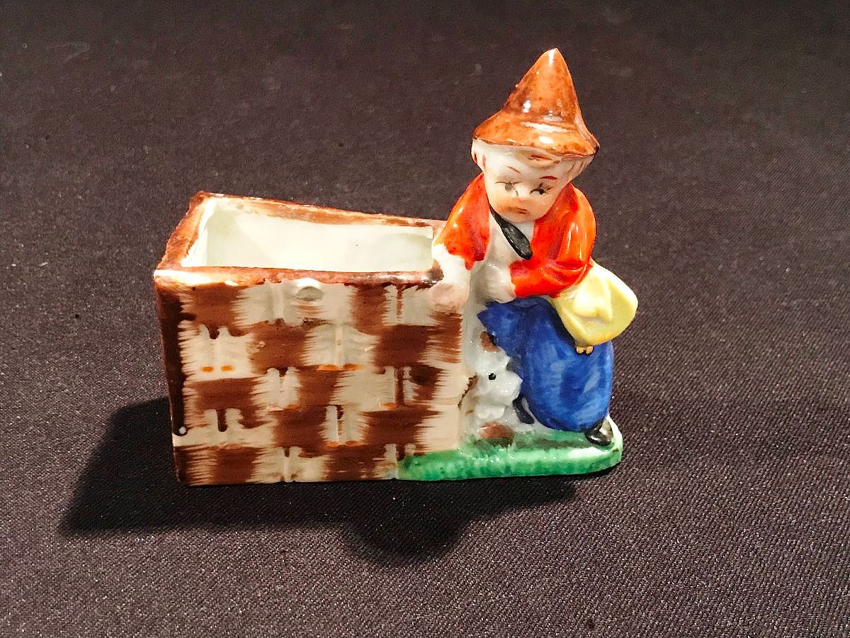 The 1930s "Made in Japan" figurine depicting a boy with a dog and a fence is a common type of vintage Japanese export pottery, often produced as an inexpensive, hand-painted ceramic novelty item.