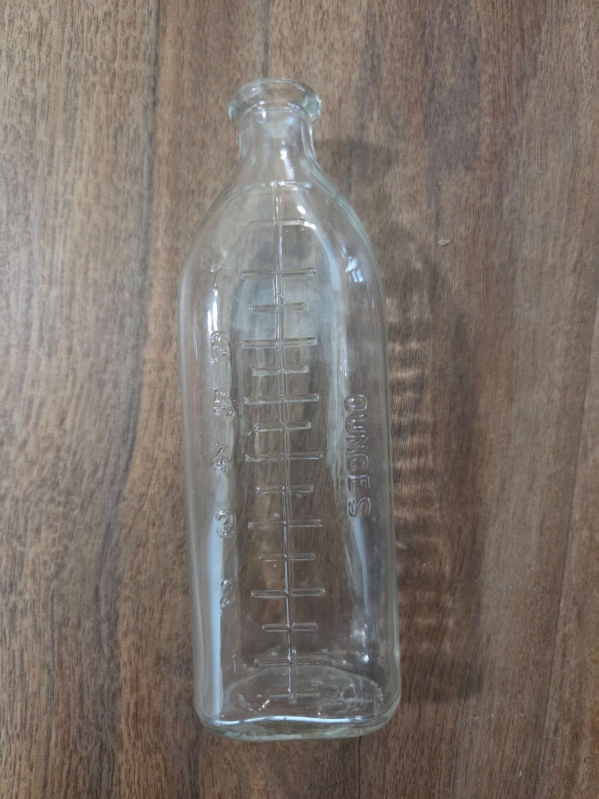 Antique clear glass narrow-neck nursing bottle with embossed ounce markings, 4oz capacity.