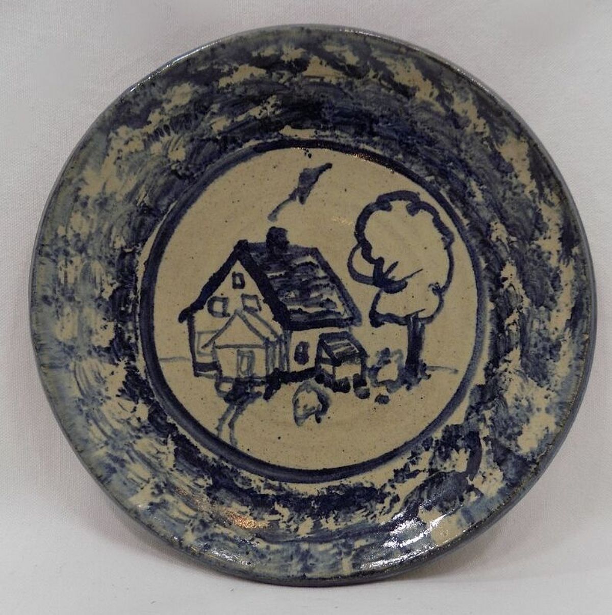 An early piece by well-known Michigan potter Carole Berhorst, this charming dish features a hand painted scene of a country cabin by a lone tree, surrounded by a sponge-decorated rim, all in blue.