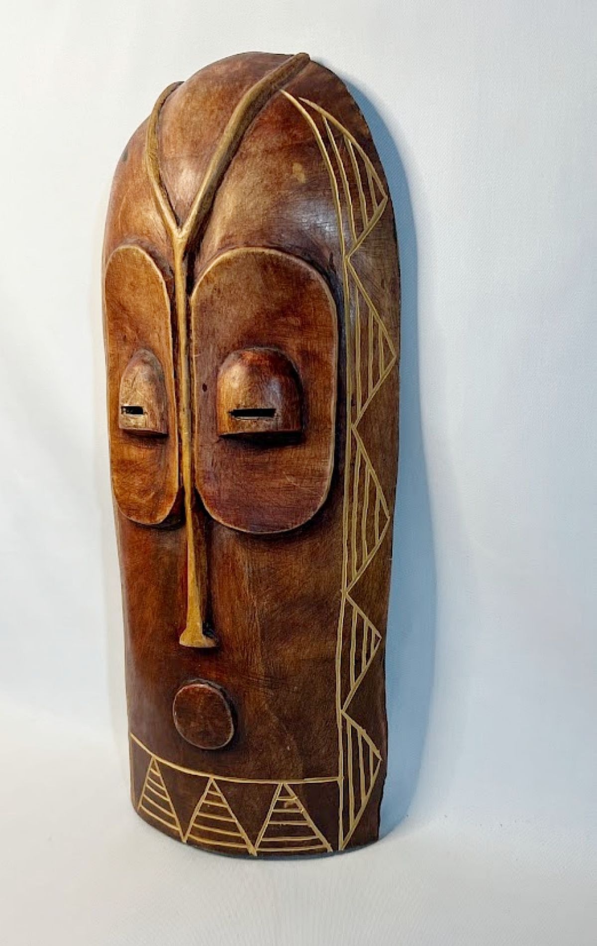 This striking large wooden mask was hand carved in Africa for sale rather than ritual use. It resembles the ceremonial masks of the Bembe people with exaggerated, owl-like eye sockets with almond-shaped, incised slits.