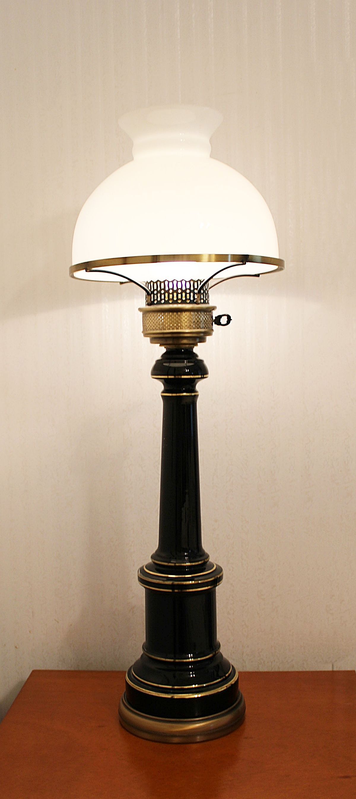 This handsome vintage electric lamp is tall and heavy. Enameled black and gold over a metal base, it has a brass bulb socket with a fancy brass key switch and a brass ring that supports the milk glass shade.