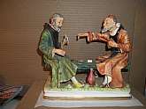 Delightful plateau group, unattributed, but holding to the styling of CapodiMonte, from the era of 1950. Two monks, with a jug of wine, indulging in a game of cards on a simple bench. Apparently one of them has discovered the other "cheating", a